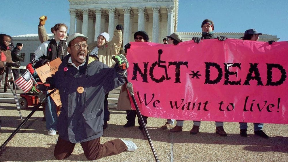 Protestors with a sign reading "Not Dead We Want To Live!"