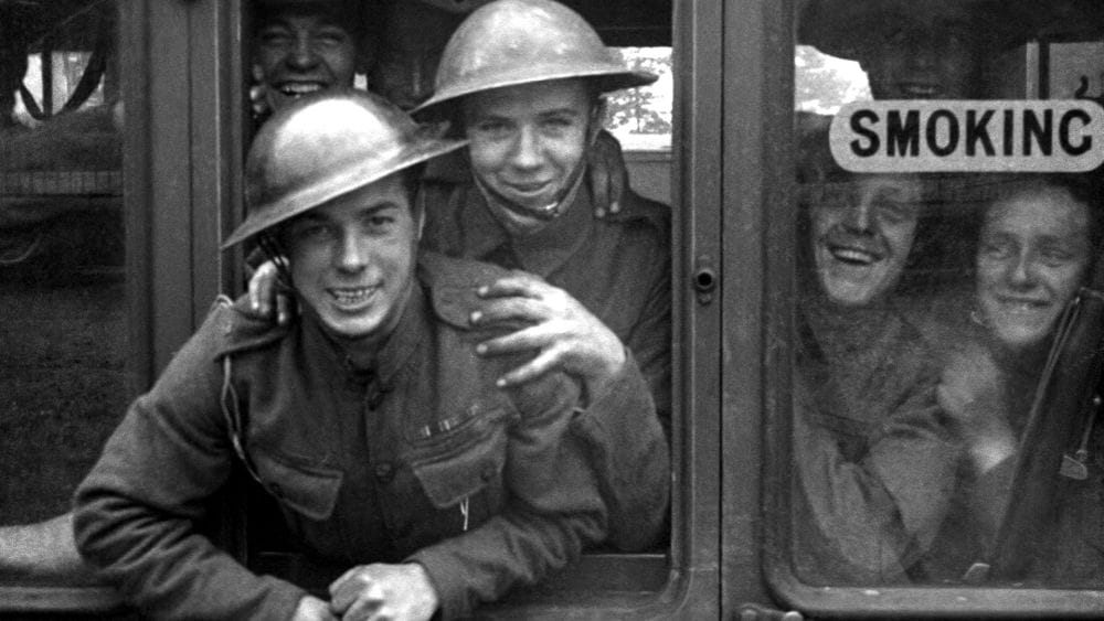 Soldiers in uniform hang out of the open window of a train.